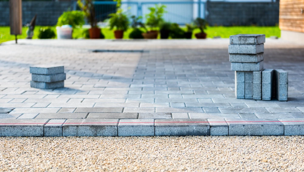 Gray paver patio installation in progress with stacked blocks and a straight guide line.