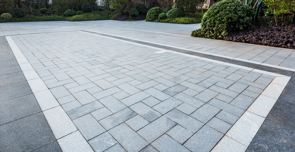 Large paver patio with geometric stone pattern bordered by landscaped shrubs.