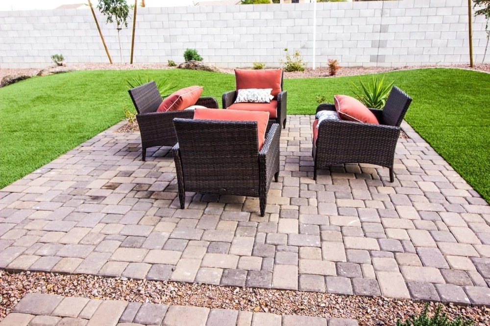 Backyard paver patio with wicker seating and coral cushions surrounded by bright green grass.