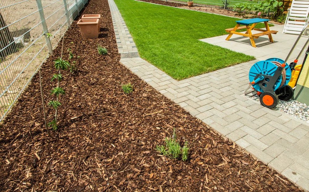 Fresh bark mulch borders a green lawn with paver paths young plants and a small picnic table.